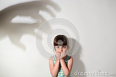 Scared small girl wearing casual sleeveless t shirt being afraid of shadows of hands on wall, looking at camera with frightened Stock Photo