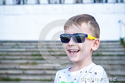 Scared surprised astonished mixed Caucasian male child with sunglasses, poses against brick white wall background Stock Photo