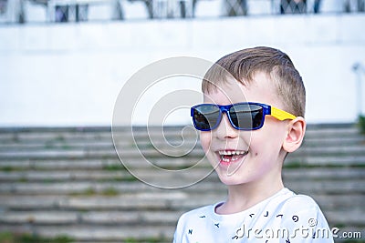 Scared surprised astonished mixed Caucasian male child with sunglasses, poses against brick white wall background. Stock Photo