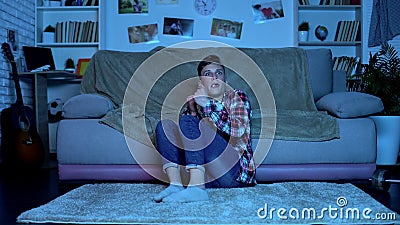 Scared teenager watching horror movie late at night, eating popcorn, emotions Stock Photo