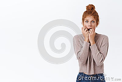 Scared, worried shocked redhead woman with curly hair in messy bun, biting fingers and stare camera frightened Stock Photo