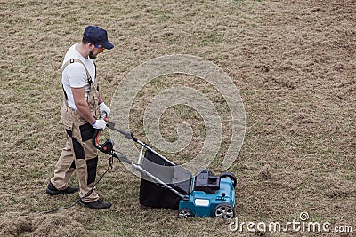 Scarifying lawn with scarifier, Man gardener scarifies the lawn and removal of old grass Stock Photo