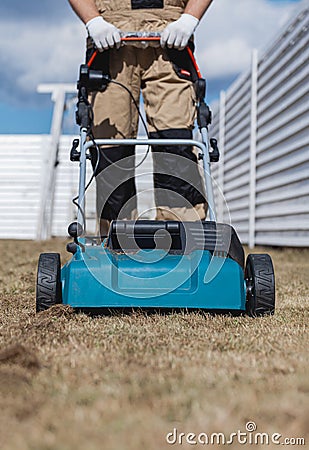 Scarifying lawn with scarifier, Man gardener scarifies the lawn and removal of old grass Stock Photo