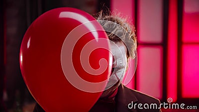 A scary clown peeking out from the red balloon and creepy smiling Stock Photo