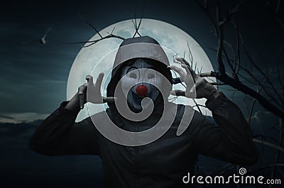 Scary evil clown wear jacket over bird, dead tree, moon and spooky cloudy sky Stock Photo