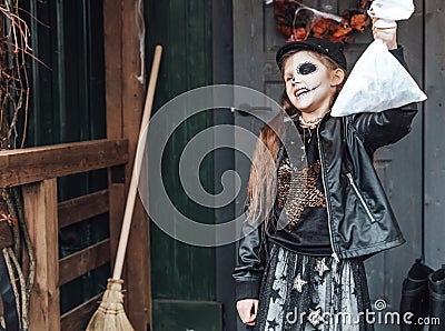 Scary girl celebrating halloween. Playing treak or treat game on porch with garland. Bag with sweets in hands Stock Photo