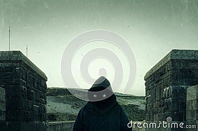 A scary, hooded figure with glowing evil eyes and blank black space where his face should be, standing on a road in the Stock Photo