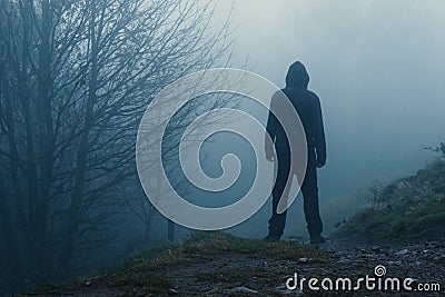 A scary hooded figure on a path through a moody misty autumn woodland Stock Photo