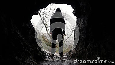 A scary horror figure, back to camera. Standing on the entrance to a cave. On a moody winters day in the countryside Stock Photo