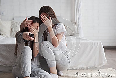 Scary moment in the horror movie. Sisters have fun watching TV while sits on the floor of beautiful bedroom at daytime Stock Photo