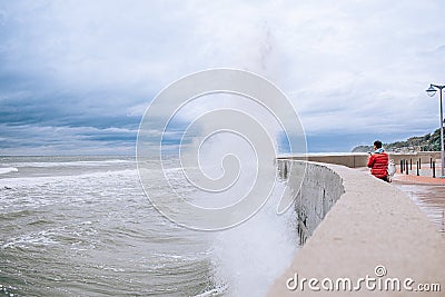 Scary Stormy Waves with Big Sea Wave Splashing Over pier Road at cloudy autumn day. Woman in red jacket shooting the wave Editorial Stock Photo
