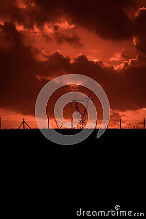 Scary sunset, with red sky and clouds, after storm. Power pylons and industrial fences in devastated landscape. B Evil environment Stock Photo