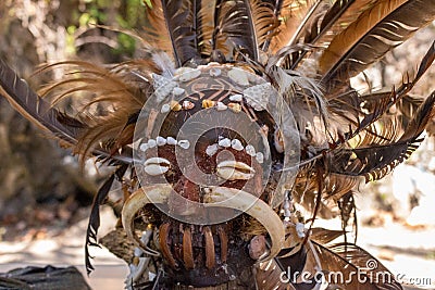 Scary wooden mask of asian totem. Head of ritual sculpture. Ancient religious mask with feathers. Stock Photo