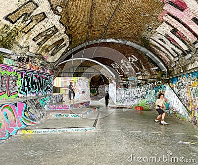 Scateboarders under London Railway Arch covered in Graffiti. Editorial Stock Photo