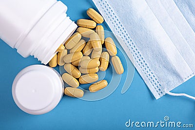 Scattering yellow pills with white medical bottle and medical mask on blue background, prevention, protection from virus concept Stock Photo