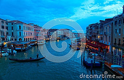 Scenery of romantic Venice in blue dusk, with tourists riding in a gondola on Grand Canal & ferry boats parking by restaurants Editorial Stock Photo