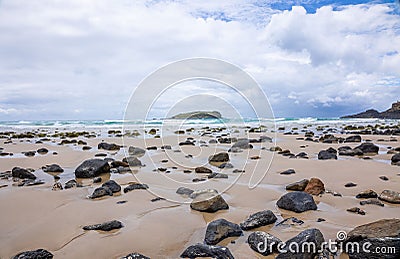 Scenic beach landscape with a serene shoreline with rocks scattered along the golden-hued sand Stock Photo