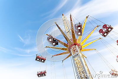Scenic bottom view high chain swing flying carousel against blue sky. Merry go round roundabout chairoplane at portable Stock Photo