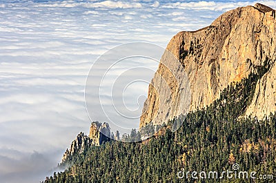 Scenic landscape of sunset autumn forest of pine trees above shroud of low scattered clouds in Caucasus Mountains. Bolshoy Tkhach Stock Photo