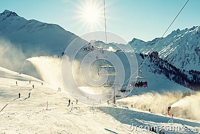 Scenic panoramic view of alpine peaks with ski lift ropeway on hilghland mountain winter resort and snow making machines on bright Editorial Stock Photo