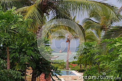 Scenic resort hotel view with palm trees and pool. Exotic landscape with boats with red sailboat and tropical garden. Stock Photo