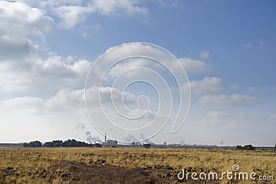 Scenic shot of a meadow and factories working in the background with smoke coming out of there Stock Photo