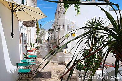 Scenic sight of the Ostuni town sunny street with typical restaurants and blooming flowers, Apulia region, Italy, Adriatic Sea Editorial Stock Photo