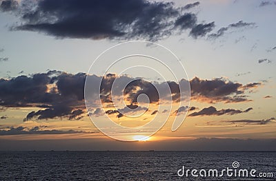 Scenic sunset over the sea. The sun sets on the water. Clouded sky is painted with bright colors. Sunset beach in a summer evening Stock Photo