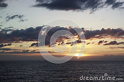 Scenic sunset over the sea. The sun sets on the water. Clouded sky is painted with bright colors. Sunset beach in a summer evening Stock Photo