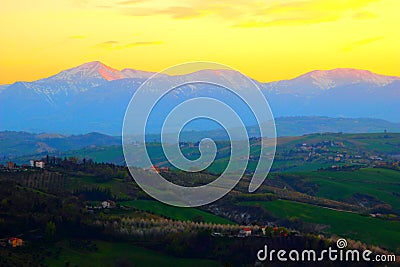 Scenic view from above at hills and mountains under the yellow sunset sky in Monte Vidon Corrado Stock Photo