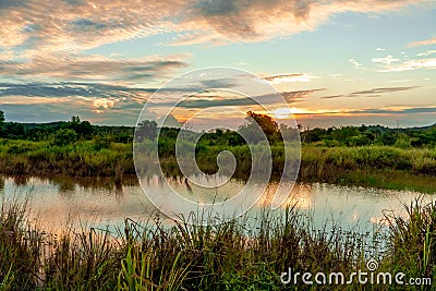 Scenic view of beautiful sunset above the lake at summer cloudy sky and grass field. Landscape of sunset and blue sky reflected on Stock Photo