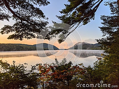 Scenic view of green forest and hills reflecting on a tranquil lake at a foggy sunset Stock Photo