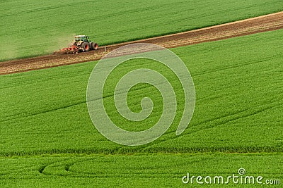 Scenic View Of Modern Farming Tractor Which Plowing Green Field. Agriculture Tractor Cultivating Wheat Field And Creating Green Ab Stock Photo