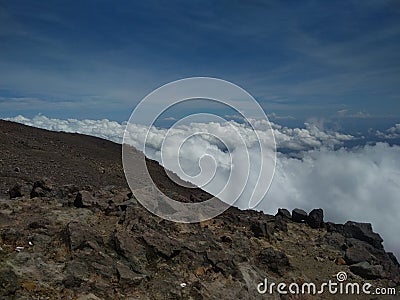 Scenic view of a rocky mountain slope above the clouds under the blue sky Stock Photo