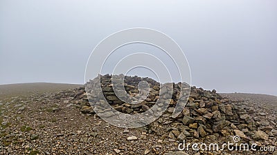 A scenic view of a rocky mountain summit with a stony cairn under a misty sky Stock Photo