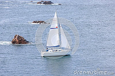 A scenic view of a sailboat along the rocky Moray Scottish coast on a calm sea Stock Photo