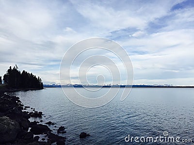 Scenic view of a serene lake shore against a backdrop of a bright blue sky and snow-capped mountains Stock Photo