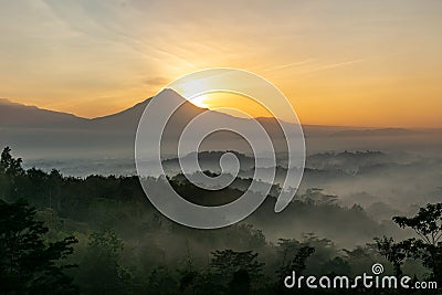 Scenic view of sunrise behind Merapi volcano, misty jungle and Borobudur temple in Indonesia Stock Photo