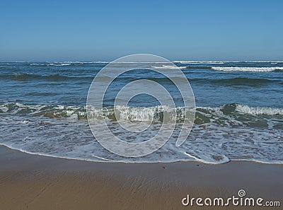 Scenic view turquoise blue breaking sea waves with white foam approaching the golden sand beach at wild Rota Vicentina Stock Photo