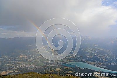 A scenics view of a mountain summit with a majestic double rainbow and Embrun, Hautes-alpes, France in the background under a Stock Photo