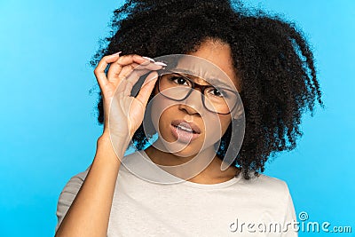 Sceptical mistrustful African American girl adjusts glasses, suspicious looking at camera. Studio. Stock Photo