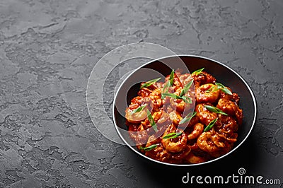 Schezwan Prawns in black bowl at dark slate background. Schezwan Prawns is indo-chinese cuisine curry dish Stock Photo