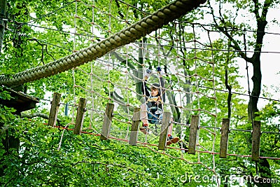 School boy in forest adventure park. Acitve child, kid in helmet climbs on high rope trail. Agility skills and climbing Stock Photo