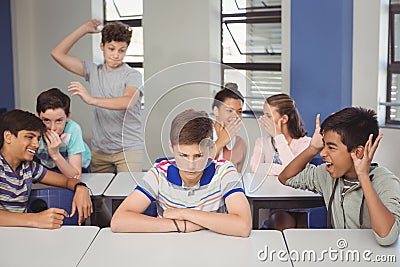 School friends bullying a sad boy in classroom Stock Photo