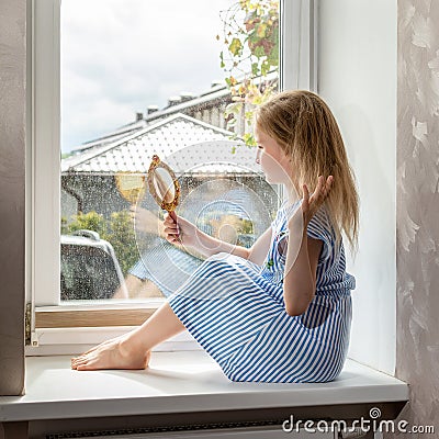 School girl combs her hair sitting on the windowsill, rainy weather outside Stock Photo