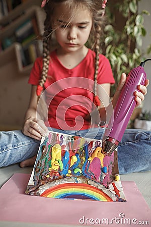 Girl draws rainbow with melted crayon pencils, she using blow dryer and wax stars to melt, art idea Stock Photo