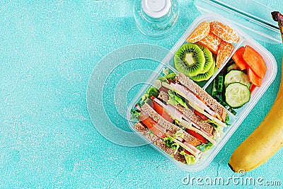 School lunch box with sandwich, vegetables, water, and fruits on table. Stock Photo