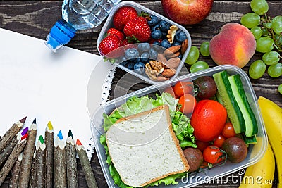 School lunch boxes with sandwich, fruits, vegetables and bottle of water with colored pencils and empty copybook Stock Photo