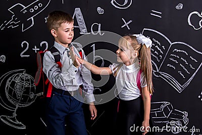 School mates standing before the chalkboard as a background with a backpack on their backs claping their hands looking Stock Photo