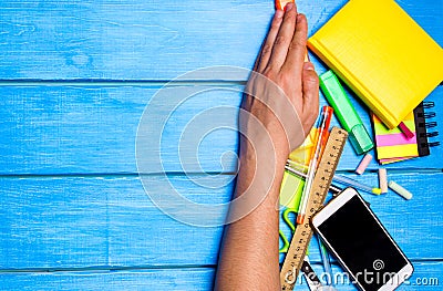 school students hand cleans away the school supplies on blue wooden table background. student prefers to perform other tasks. Stock Photo